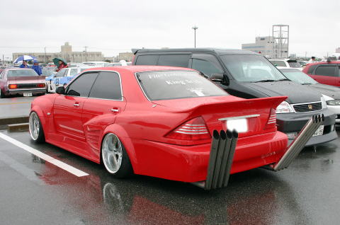 red sedan with large exhaust pipes and spoiler, parked next to a black van and other cars