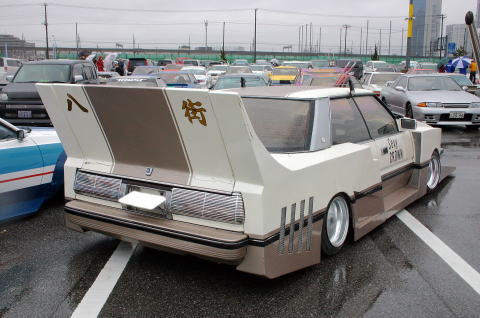 Modified sedan, cream and brown, with a massive rear wing and custom body kit, viewed from the rear