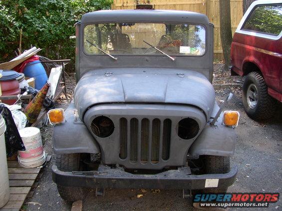 Gray Jeep CJ5 front view, primer finish, missing headlights, parked next to a red SUV