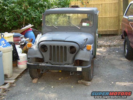 Gray Jeep truck with a flat grille and round headlights, parked on blocks