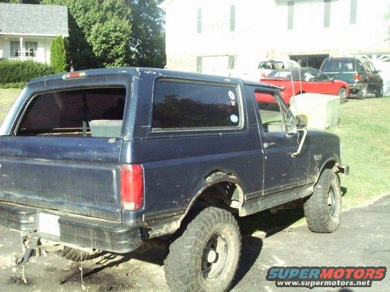 1992 Ford Bronco with large off-road tires parked in a driveway, other vehicles visible in background