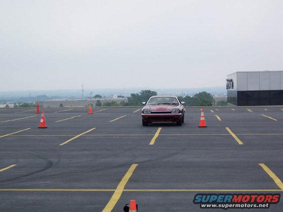 red coupe driving through cones in an empty parking lot