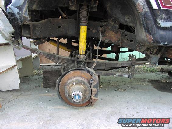 Close-up of a truck's rear suspension with leaf springs and a disc brake assembly. Yellow shock absorber visible