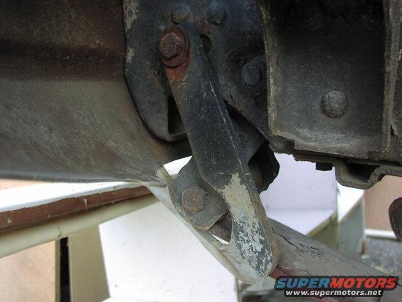 Undercarriage bracket with rust and peeling paint, attached to a vehicle frame