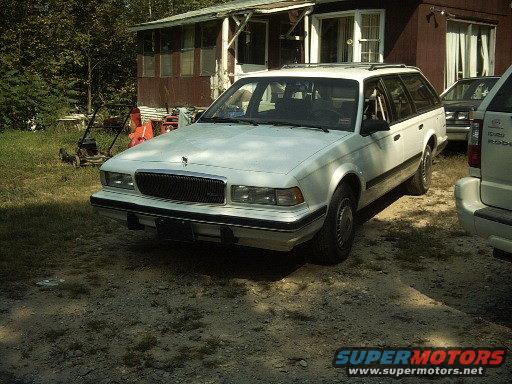 White station wagon parked in front of a house, with another vehicle to the right
