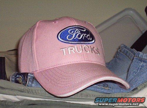Pink baseball cap with blue Ford oval logo and 'TRUCKS' text, resting on clothes