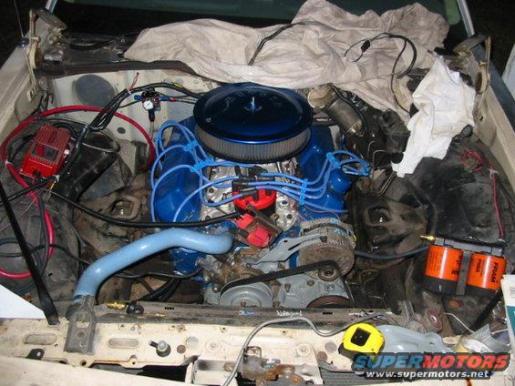 engine bay with blue valve covers, air filter, and various hoses and wires