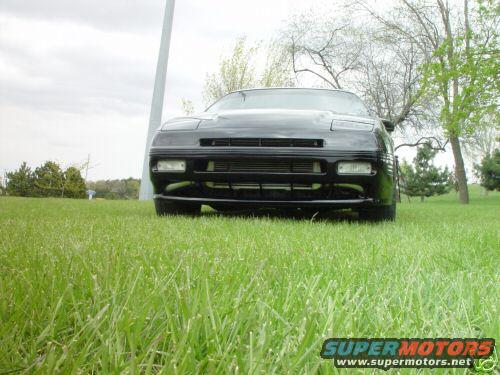 Black car front view, parked on grass with trees and a tall pole in the background