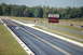 2005 Ford Deluxe - Cars race down a drag strip under a scoreboard displaying elapsed times.