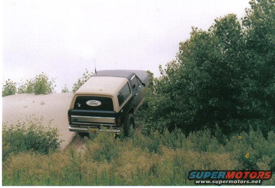 Ford Bronco driving on a sandy hill next to trees
