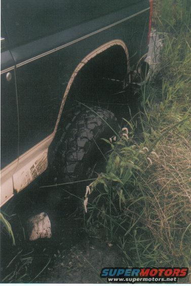 Dark SUV rear wheel well and tire in tall grass