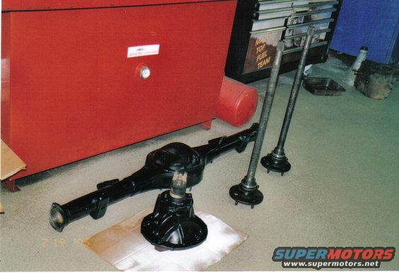 Black rear axle assembly and three axle shafts on a garage floor