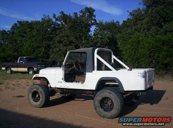 White Jeep CJ-series with black soft top and roll cage, lifted suspension, off-road tires, seen from 3/4 front angle