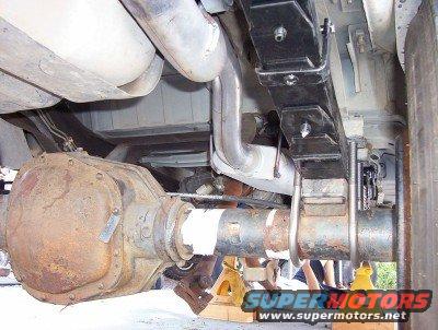 Underside of vehicle showing rear axle, leaf springs, and exhaust pipes. Vehicle is on jack stands