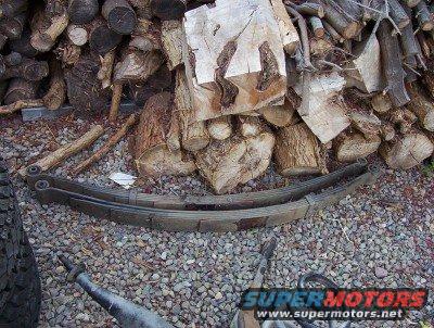 Leaf springs on gravel with stacked firewood in the background