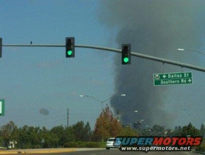 Traffic lights with green signals against a blue sky with a large smoke plume rising in the distance