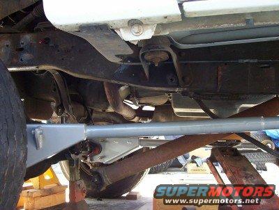 Underbody of a vehicle on jack stands, showing frame, suspension, and exhaust components