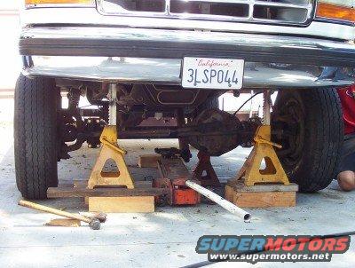 Ford truck front end raised on jack stands, showing suspension and undercarriage. California license plate 3LSP044