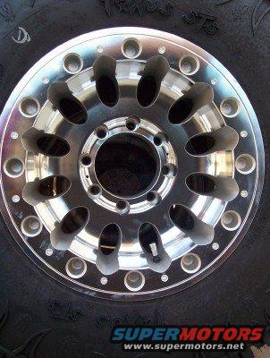 Custom aluminum wheel with large lug holes on a tire. "SUPERMOTORS" text visible