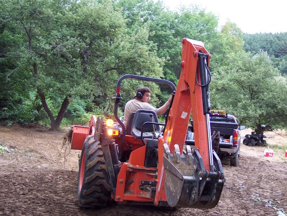 Orange tractor with backhoe attachment, rear view. Pickup truck and ATV in background