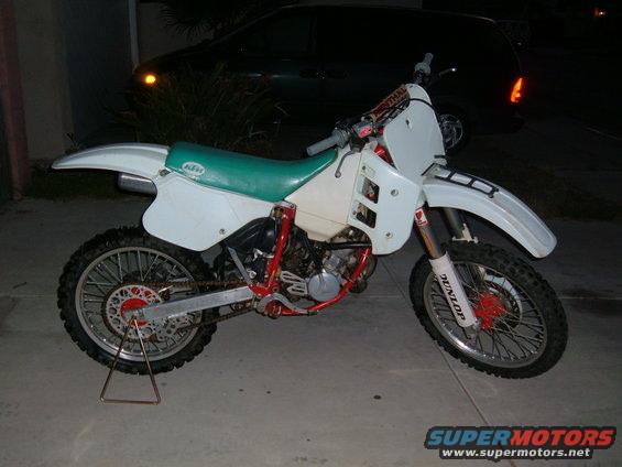 White dirt bike with a green seat and red frame, on a kickstand