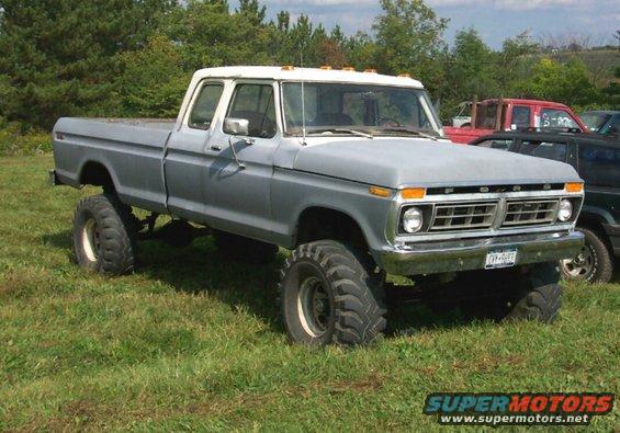 1979 Ford F-150 pickup truck with large tires and lift kit parked on grass, other vehicles visible behind