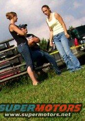 guy sitting with two women standing near a dark SUV