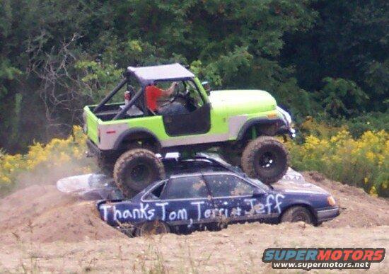 Green off-road vehicle on top of a dark sedan with writing on its side