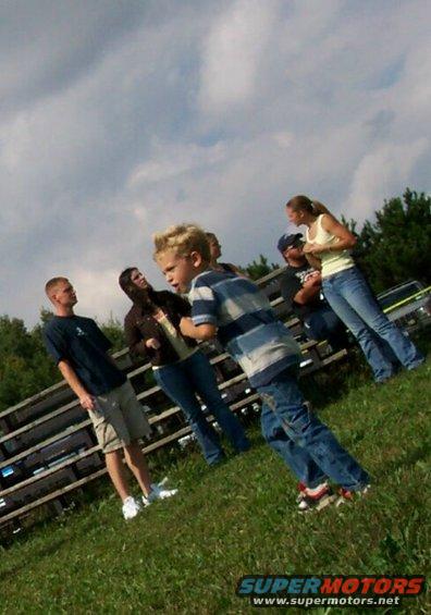 Group of people, including a young boy in a striped shirt, standing on a grassy hill under a cloudy sky