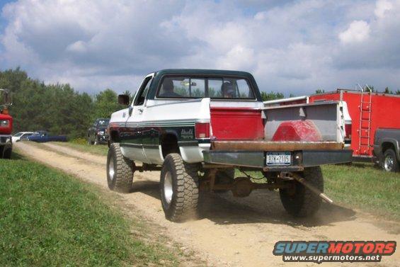 Rear view of lifted white and green pickup truck with flatbed, license plate RZK-2105