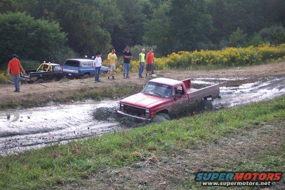 red pickup truck stuck in mud, other trucks and people watching