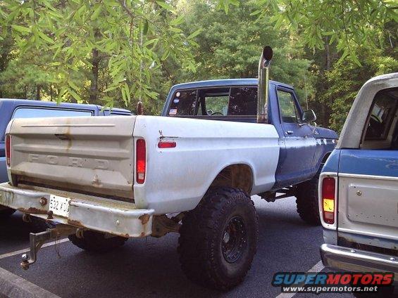 Rear view of a lifted Ford pickup truck with a large chrome exhaust stack, parked next to another vehicle