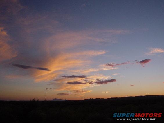 Sunset with colorful clouds over a dark, silhouetted landscape. A single pole stands in the middle ground