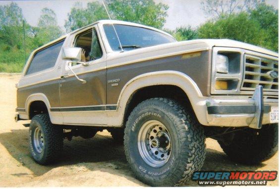 1982 Ford Bronco, two-tone brown and white, parked on dirt with trees in background
