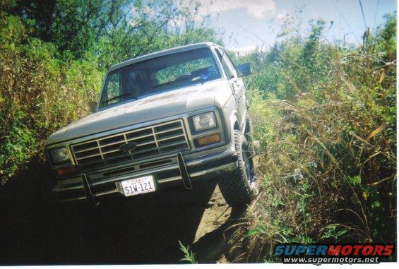 Ford Bronco driving on a dirt path with brush on both sides