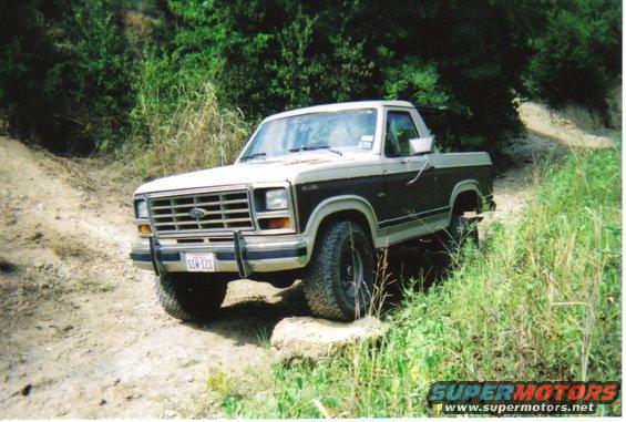 Two-tone brown and white Ford Bronco on a dirt path with rocks