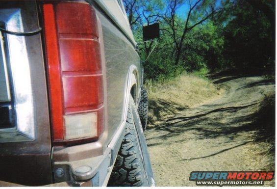Rear of a brown Ford Bronco on a dirt road, showing the taillight and tire