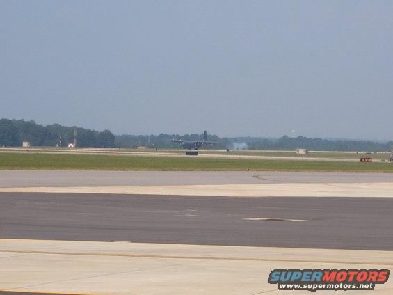 Military transport aircraft on an airport runway, with smoke trailing