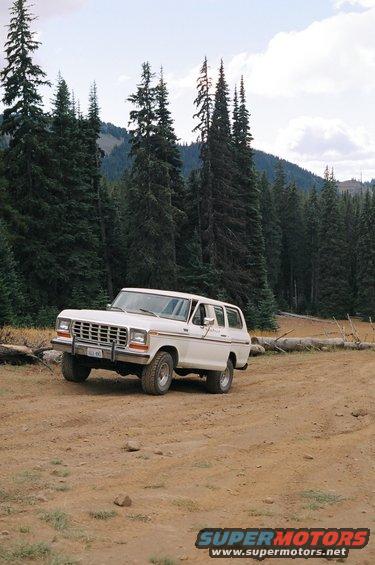 White 1978 Ford Bronco SUV parked on a dirt road with pine trees and mountains in the background