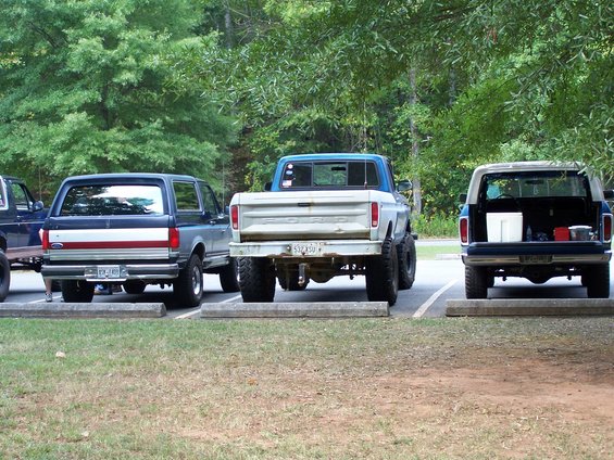 Rear view of a lifted 1970s Ford pickup truck parked next to two Ford Broncos