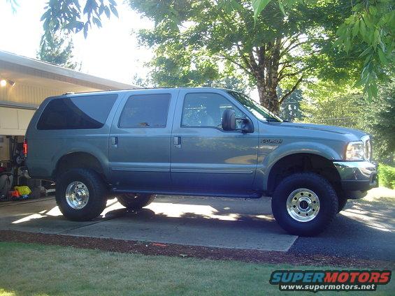 Gray Ford Excursion parked outside a garage. Lifted suspension and large tires