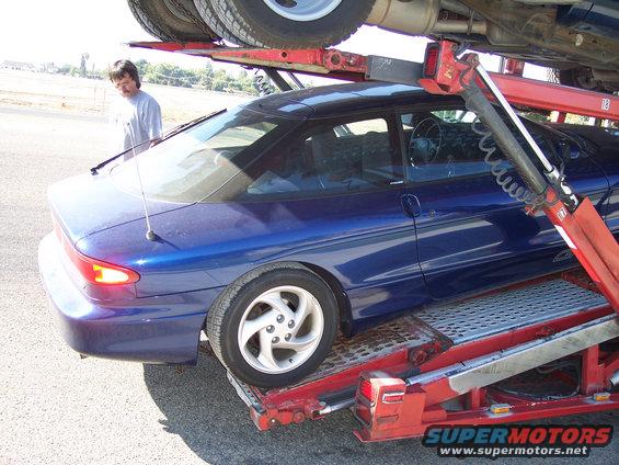 Blue coupe being loaded onto a car carrier. A man stands nearby