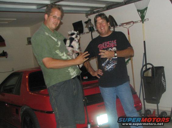 guy holding dog next to red car in garage