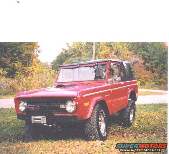 Red Ford Bronco parked on grassy area with trees in background