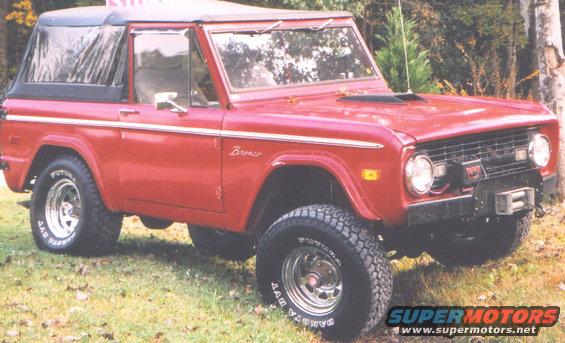 Red 1974 Ford Bronco with a black soft top, chrome wheels, and a winch on the front bumper