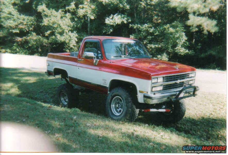 Red and white lifted pickup truck with chrome grille and off-road tires