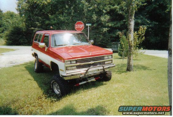 Red and white Chevrolet K5 Blazer parked on grass with a stop sign behind it