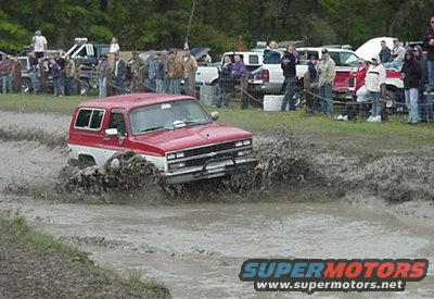 red and white SUV driving through mud pit, spectators watching