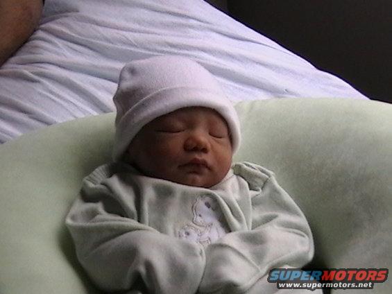 Baby wearing a white hat and light green onesie, sleeping in a green pillow