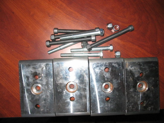 Four metal plates with bolts and nuts on a wooden surface